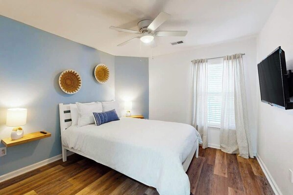 A bedroom with a bed, a ceiling fan, a TV, and a window with curtains. - The Fairways Unit 19D (Myrtle Beach)
