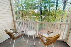 A porch with two wicker chairs and a small table, overlooking a forested area. - The Fairways Unit 19D (Myrtle Beach)