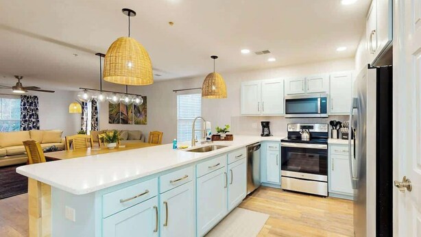 A modern kitchen with light blue cabinets, stainless steel appliances, and pendant lighting. - The Fairways Unit 19D (Myrtle Beach)