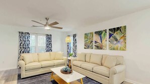 A living room with two sofas, a coffee table, a ceiling fan, and abstract wall art. - The Fairways Unit 19D (Myrtle Beach)