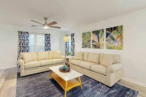 A living room with two sofas, a coffee table, a ceiling fan, and abstract wall art. - The Fairways Unit 19D (Myrtle Beach)