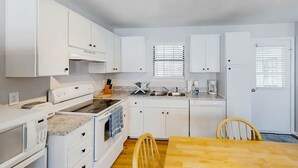 A compact kitchen with white cabinetry, a built-in oven, a sink, and a dining area with a wooden table and chairs. - 3rd Avenue Oasis Retreat (North Myrtle Beach)