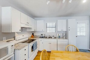A compact kitchen with white cabinetry, a built-in oven, a sink, and a dining area with a wooden table and chairs. - 3rd Avenue Oasis Retreat (North Myrtle Beach)