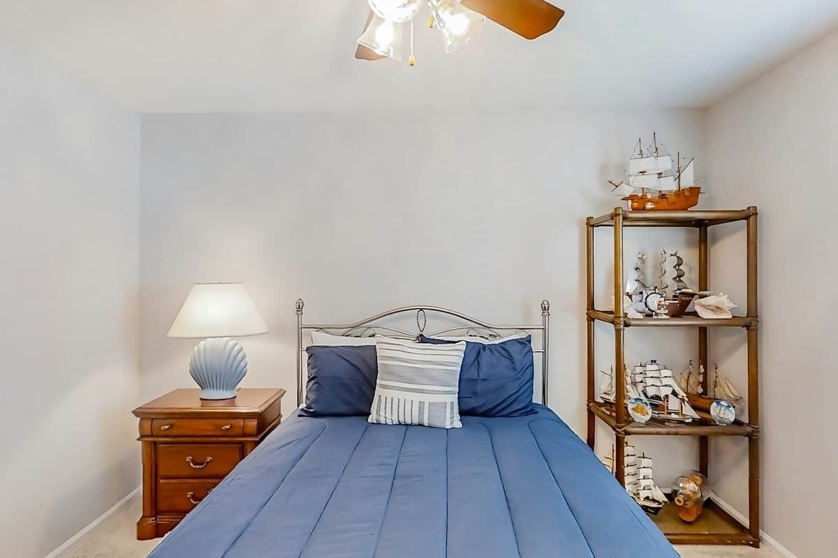 A bedroom with a bed, a nightstand, a lamp, and a shelf with decorative items.