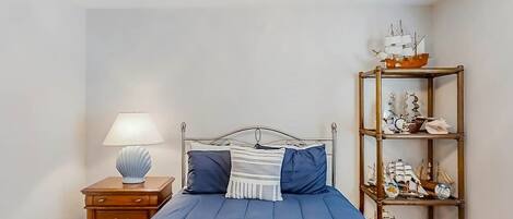 A bedroom with a bed, a nightstand, a lamp, and a shelf with decorative items.