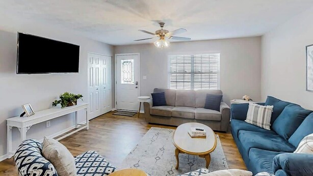 A living room with a flat-screen TV, a ceiling fan, a sofa, a coffee table, and a bench. - 3rd Avenue Oasis Retreat (North Myrtle Beach)