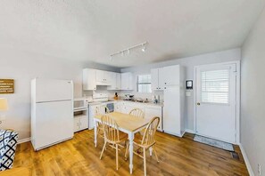 Eine kleine Küche mit weißen Schränken, einem Esstisch mit Stühlen und einem Kühlschrank.