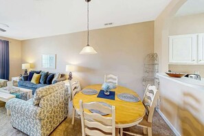 Een woonkamer met een bank, een eettafel met stoelen, een lamp en een keuken met kastjes.