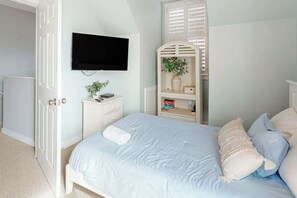 A bedroom with a bed, a TV mounted on the wall, a bedside table with a plant, and a built-in shelving unit. - 34 Compass Ct Retreat (Pawleys Island)