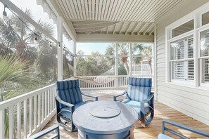 A covered outdoor seating area with a round table and blue chairs, surrounded by a white railing and palm trees. - 34 Compass Ct Retreat (Pawleys Island)