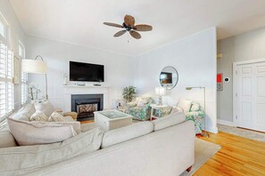 A living room with a sofa, armchairs, a television, a fireplace, and a ceiling fan. - 34 Compass Ct Retreat (Pawleys Island)
