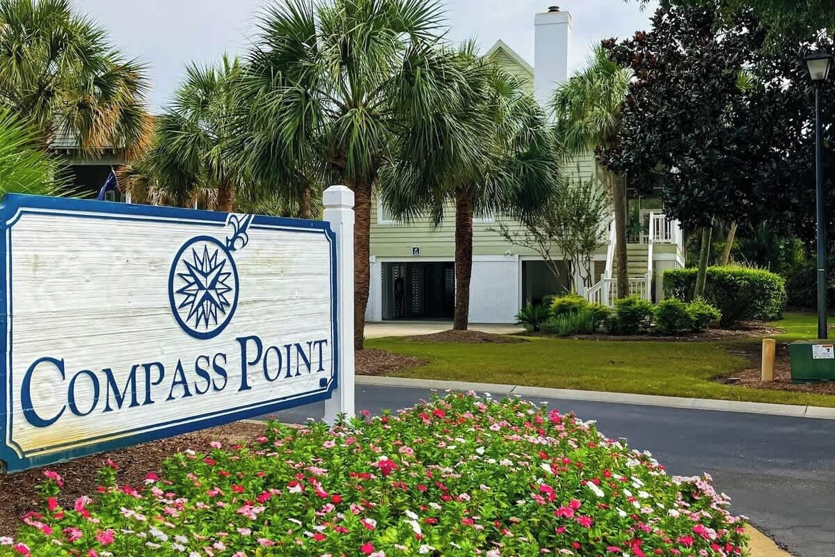 A sign for Compass Point with a palm tree and building in the background.