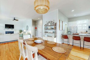 A modern kitchen with white cabinets, a wooden dining table with placemats, and a hanging light fixture. - 34 Compass Ct Retreat (Pawleys Island)