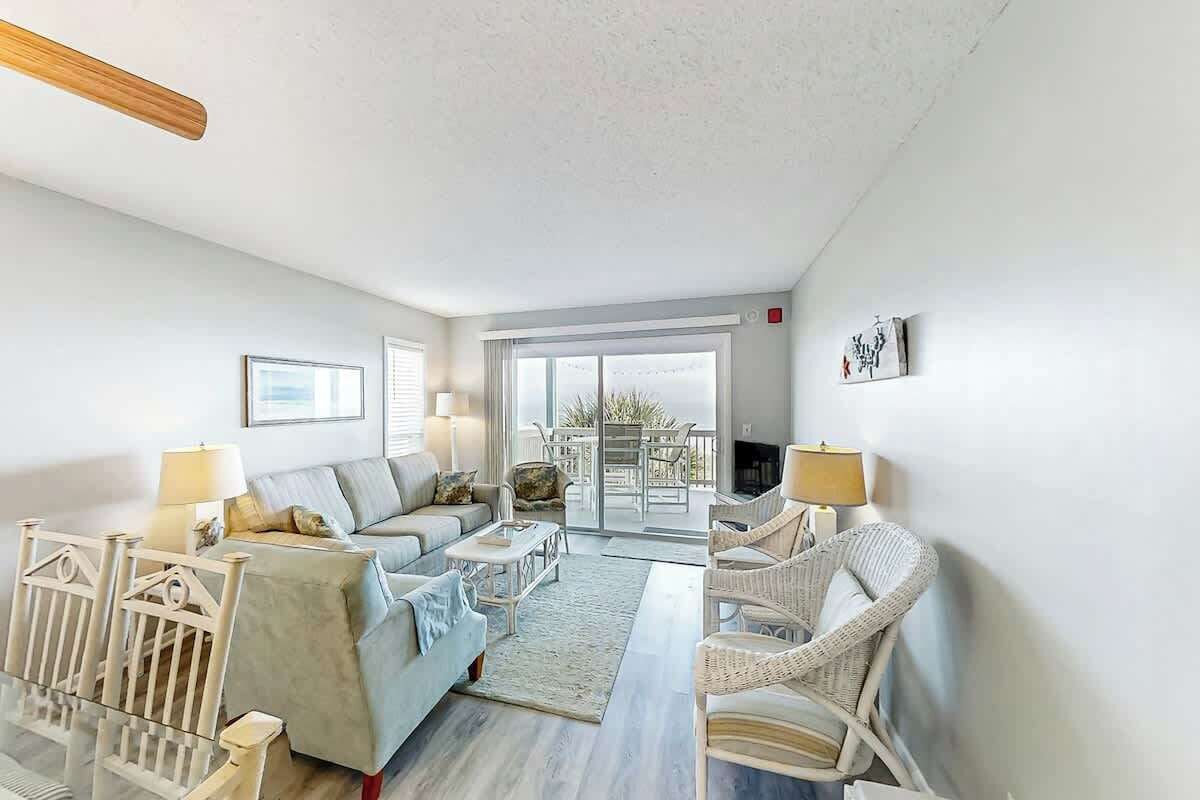 Amplia sala de estar con sofá, sillas, una mesa de centro de vidrio y vista al exterior a través de una puerta corrediza.