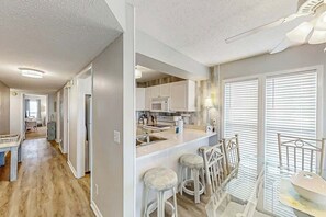 A modern kitchen with a central island, bar stools, and a dining area with a table. - Windcrest Villas 201 (North Myrtle Beach)