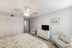 Un dormitorio con cama, cómoda, televisión, silla y ventilador de techo.