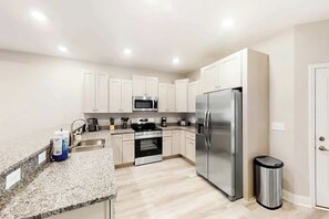 A modern kitchen with white cabinets, stainless steel appliances, and a granite countertop. - Cocora on Church Street - A (Myrtle Beach)