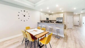 A modern kitchen with white cabinets, a central island, and a dining area with a table and chairs. - Cocora on Church Street - A (Myrtle Beach)