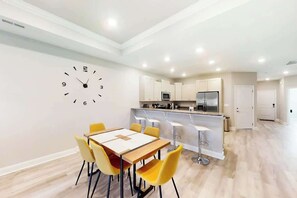 A modern kitchen with white cabinets, a central island, and a dining area with a table and chairs. - Cocora on Church Street - A (Myrtle Beach)