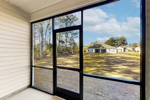 A room with large windows offering a view of a house and surrounding trees. - Cocora on Church Street - A (Myrtle Beach)