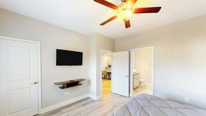 A bedroom with a bed, a ceiling fan, a TV mounted on the wall, and a door leading to a bathroom. - Cocora on Church Street - A (Myrtle Beach)