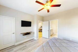 A bedroom with a bed, a ceiling fan, a TV mounted on the wall, and a door leading to a bathroom. - Cocora on Church Street - A (Myrtle Beach)