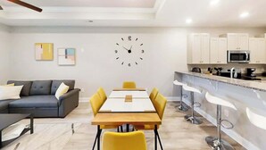 A modern living room with a sofa, a dining table, and a kitchen area with cabinets and a microwave. - Cocora on Church Street - A (Myrtle Beach)