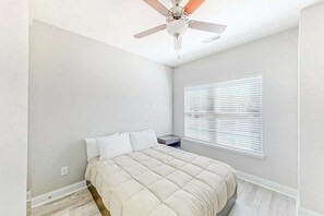 Ein Schlafzimmer mit einem Bett, einem Nachttisch, einem Deckenventilator und einem Fenster mit Jalousien.