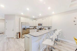 A modern kitchen with white cabinets, stainless steel appliances, and a bar area with bar stools. - Cocora on Church Street - B (Myrtle Beach)