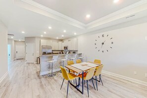 A modern kitchen with white cabinets, a central island, and a dining area with yellow chairs. - Cocora on Church Street - B (Myrtle Beach)