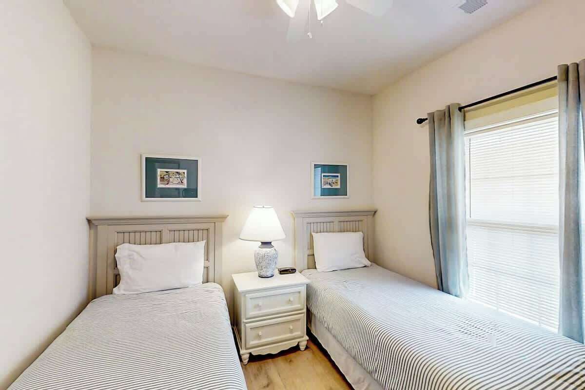 Une chambre d’hôtel avec deux lits, une table de chevet avec une lampe et une fenêtre avec des rideaux.