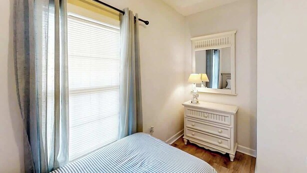A bedroom with a bed, a dresser, a mirror, and a window with curtains. - Cypress Bend Unit 432 (North Myrtle Beach)