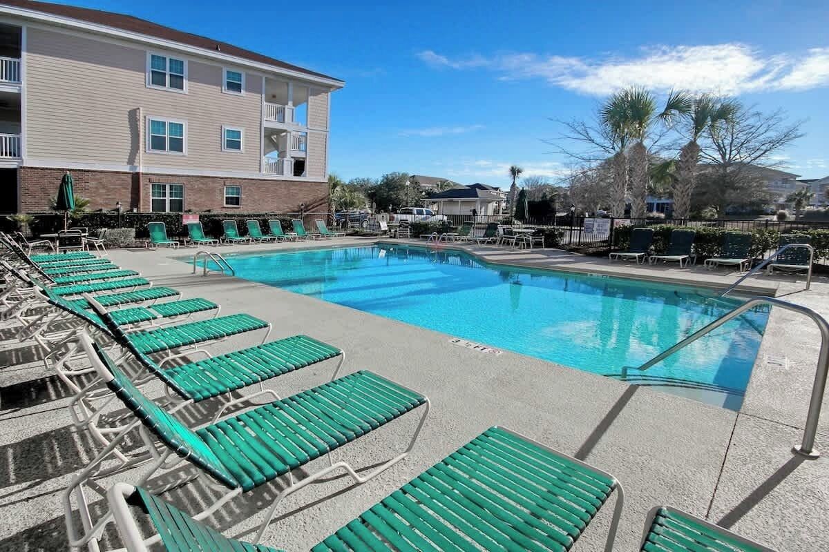 Una piscina con sillones reclinables y un edificio al fondo.