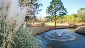 A serene water feature with a fountain, surrounded by grass and trees. - Cypress Bend Unit 432 (North Myrtle Beach)