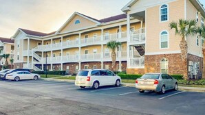 A multi-story hotel with balconies, a parking lot, and palm trees. - Cypress Bend Unit 432 (North Myrtle Beach)