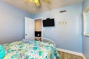 A bedroom with a bed, a television, a door, and a wall-mounted shelf. - Ocean Vibes Beach Retreat (Murrells Inlet)
