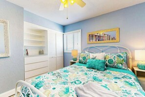 Ein Schlafzimmer mit einem Bett, einem Deckenventilator, einem Bücherregal und einem Fenster mit Jalousien.