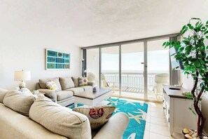 A modern living room with a sofa, coffee table, and a view of the sea through large sliding doors. - Ocean Vibes Beach Retreat (Murrells Inlet)