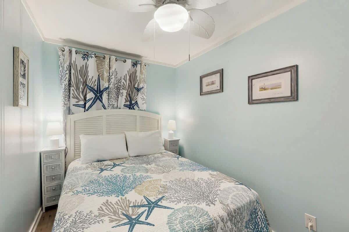 A bedroom with a bed, a nightstand, a ceiling fan, and wall-mounted artwork.