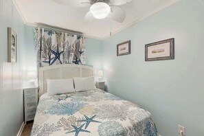 Ein Schlafzimmer mit Bett, Nachttisch, Deckenventilator und Wandbildern.