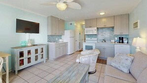 A compact living space with a kitchenette, a flat-screen TV mounted on the wall, a ceiling fan, and a sofa with decorative pillows. - Myrtle Beach Resort  A-306 (Myrtle Beach)