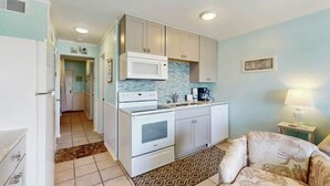 A compact kitchen with white cabinets, a microwave, and a stove. A patterned rug is on the floor, and a lamp is on a side table. - Myrtle Beach Resort  A-306 (Myrtle Beach)