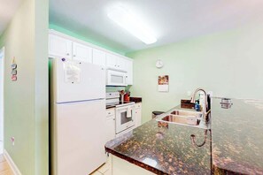 A kitchen with white cabinets, a microwave, an oven, a granite countertop, and a stainless steel sink. - The Singing Gull Retreat (Myrtle Beach)