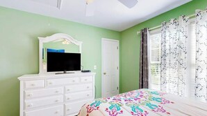 Une chambre à coucher avec un lit, une commode, un téléviseur et une porte.