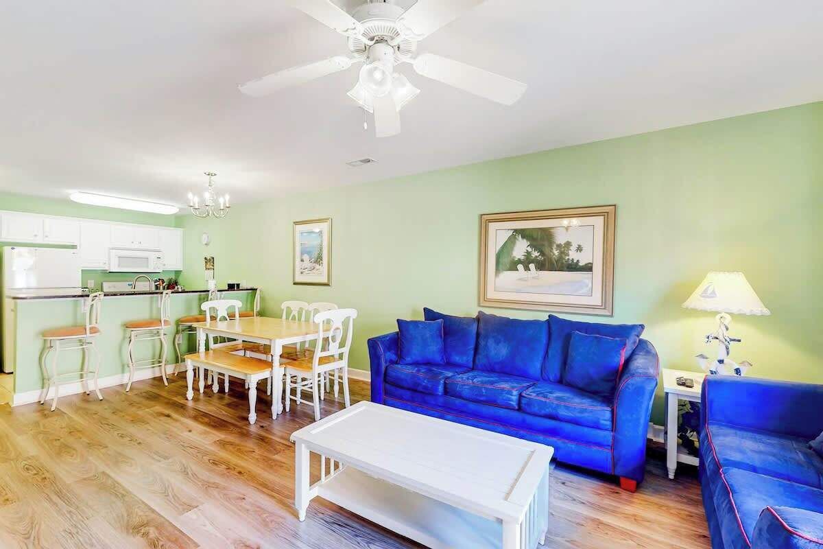 Un salon avec un canapé bleu, une table basse blanche et un coin repas comprenant une table et des chaises.