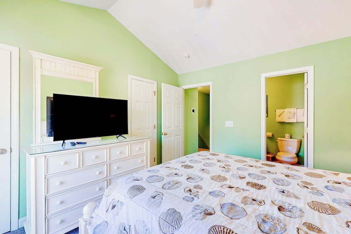 A bedroom with a bed, a television on a dresser, and a bathroom visible through an open door.