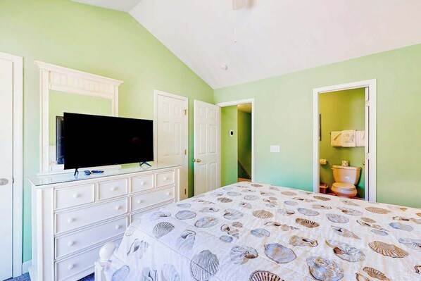 Quarto com cama, televisão sobre um penteadeira e banheiro visível por uma porta aberta.