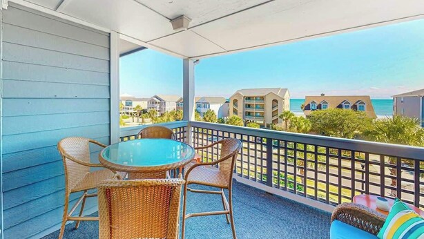A balcony with wicker furniture and a glass table, overlooking a beach with buildings in the background. - *Hook Wine and Sinker (Surfside Beach)