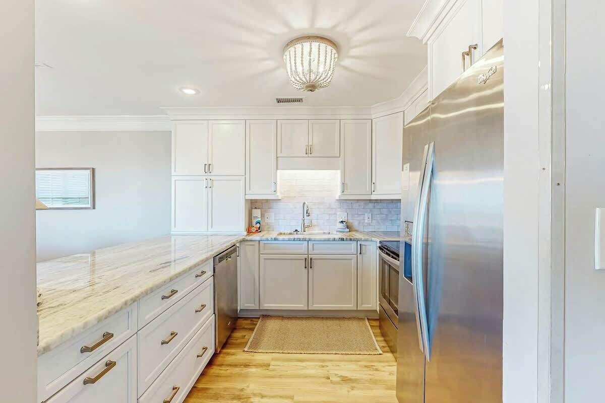 A kitchen with white cabinets, a marble countertop, a stainless steel refrigerator, and a chandelier.
