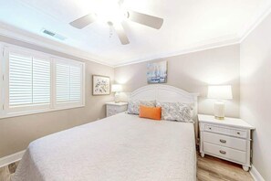 Ein Schlafzimmer mit Bett, Nachttischen, Deckenventilator und Fenster mit Jalousien.